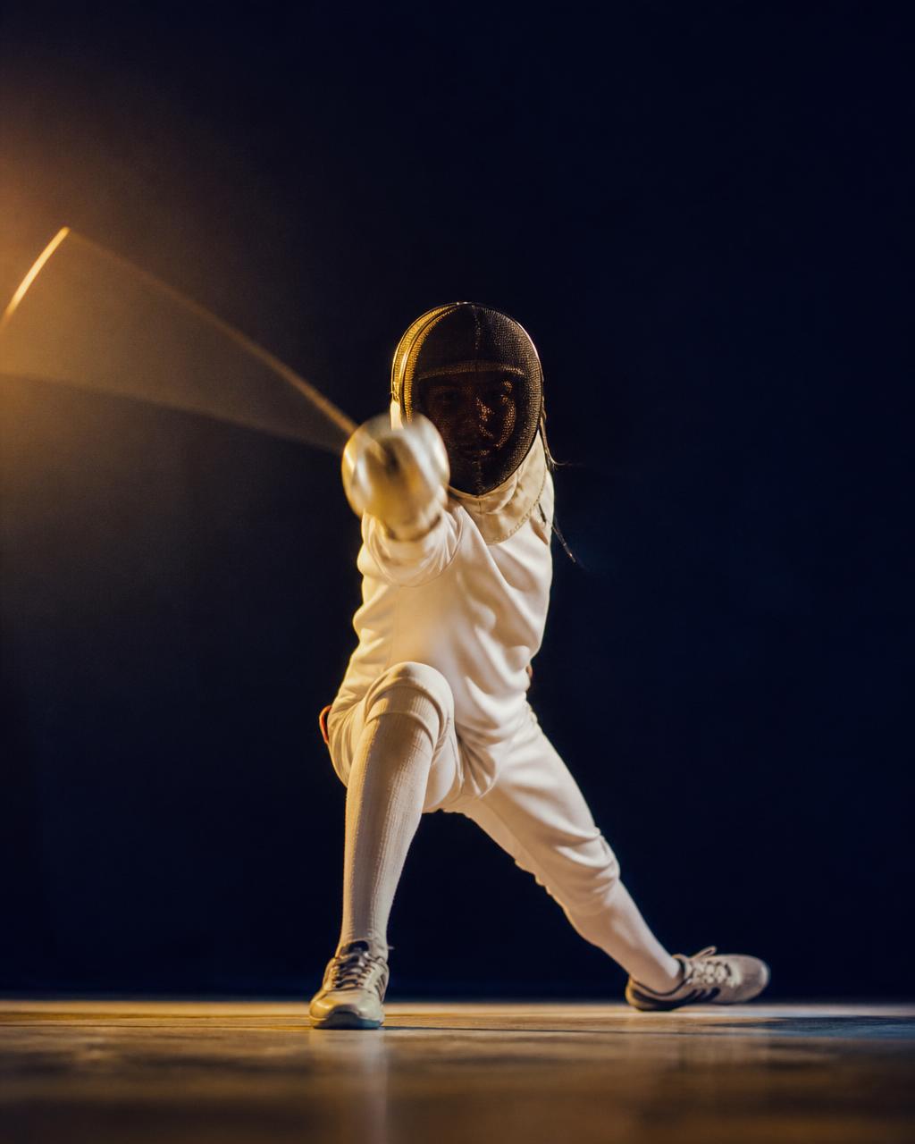 A standing fencer in white kit attacking on the piste